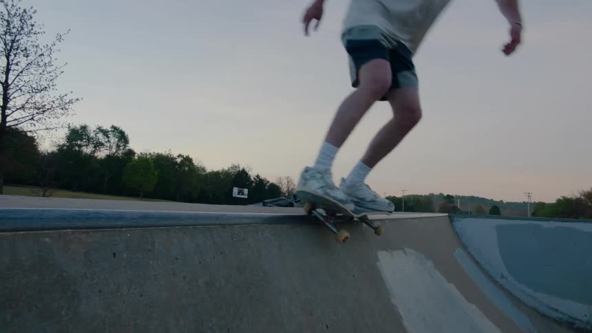 Male skateboarder performs trick in skatepark at dusk