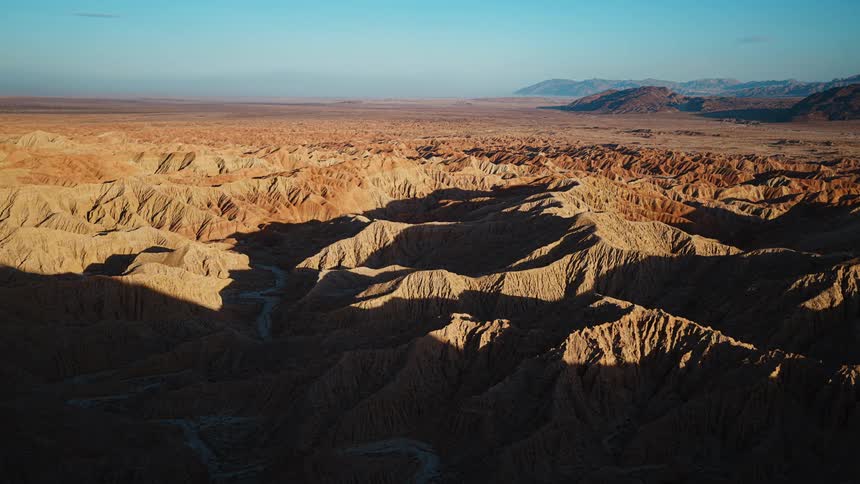The sun shines on mountains across the desert and there are mountains on the horizon under a clear hazy sky