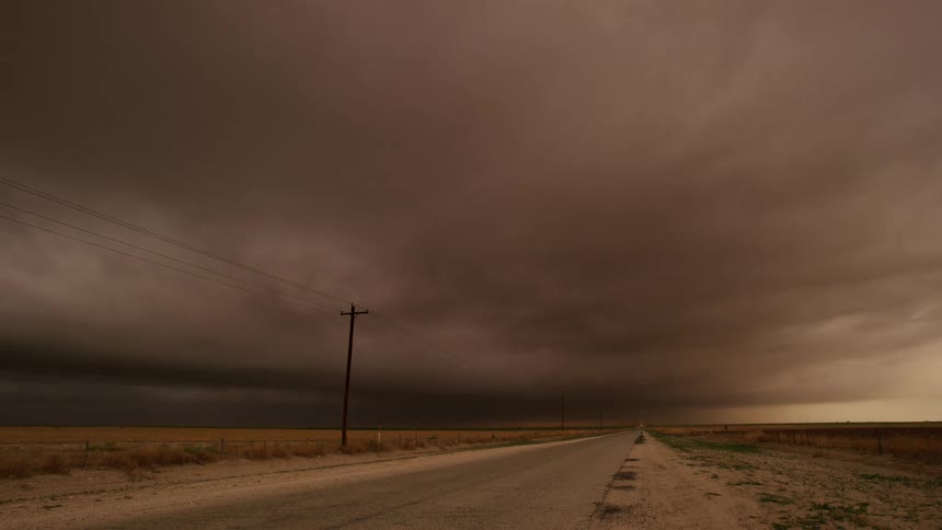 Time lapse of cars driving on a rural road under rolling storm clouds