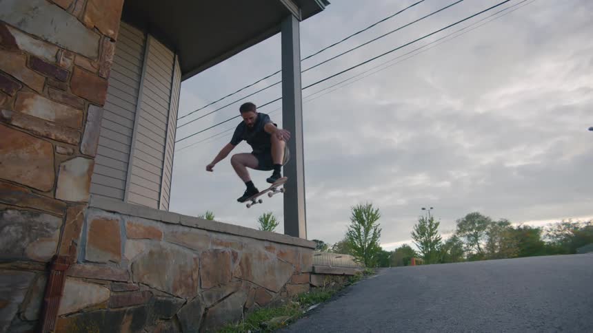 A teenage boy jump over a ledge on his skateboard in an empty parking lot