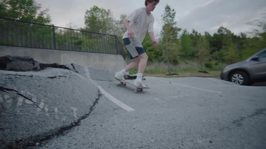 A teenage boy skates on broken asphalt in a parking lot