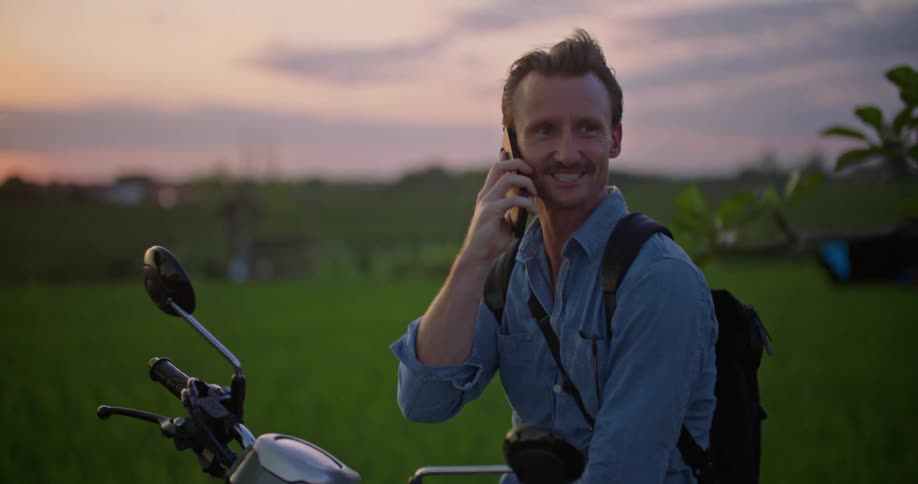 Man talking on cell phone while sitting on motorcycle in the country at sunset