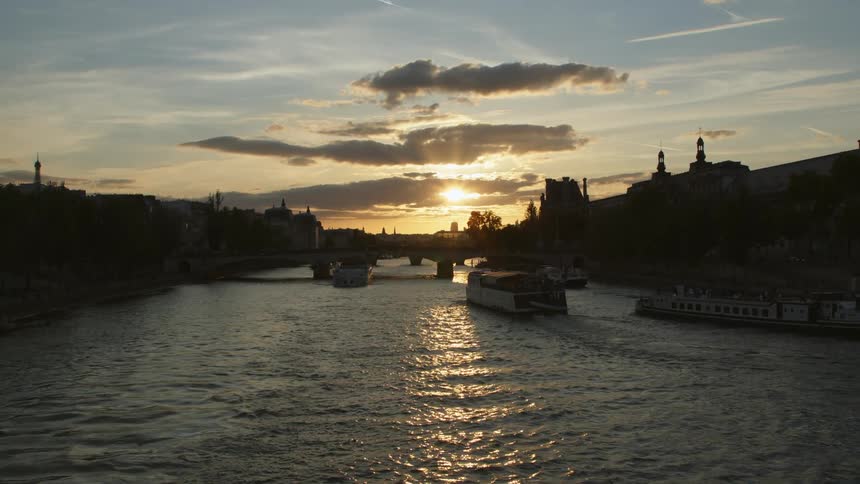 Ferries moving ahead under a bridge on a river through the silhouette of a town at evening