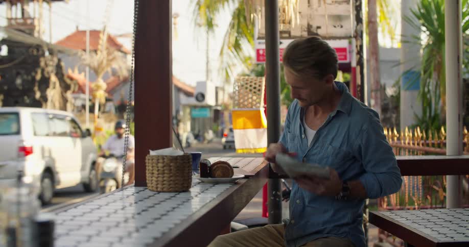 Man checks ingredients of a product on a laptop while sitting on a restaurant next to a street