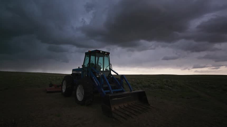 Storm cloud time lapse of a Ford tractor parked on a field under dark moving storm clouds