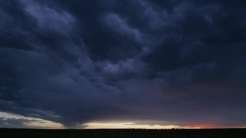 Time lapse of dark storm clouds move overhead as they reflect the red sky in the distance