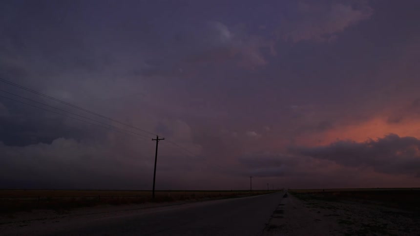 Pastel colored Time lapse of cars driving on a rural road under rolling storm clouds at nightfall that goes into dark