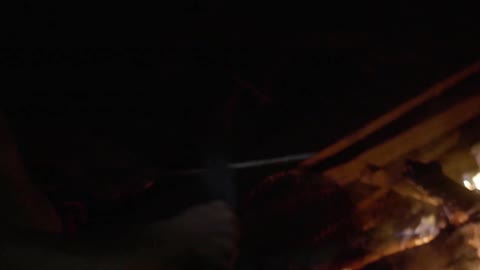A person is sharpening their blade by a fire