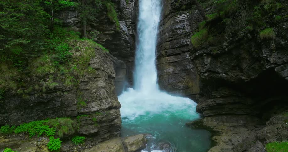 Waterfall flowing down the rugged surface of a cliff on the mountains surrounded by green lush vegetation