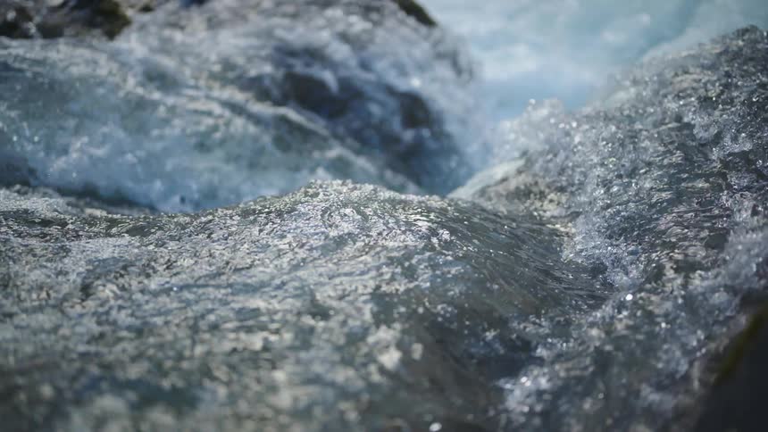 River water flowing over rock splashing and foaming as it sparkles in the sunlight