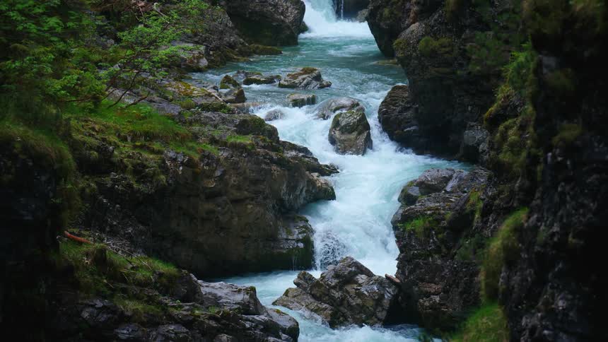 Waterfalls in a stream is rolling over rocks as it flows down the rapids surrounded by rocks covered in green moss