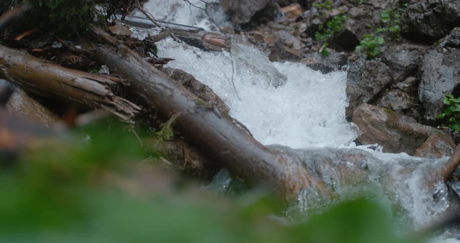 Waterfall cascades over the rocks as logs lay next to it