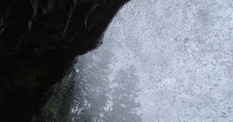View from behind a waterfall falling over the edge of a cliff in the forest