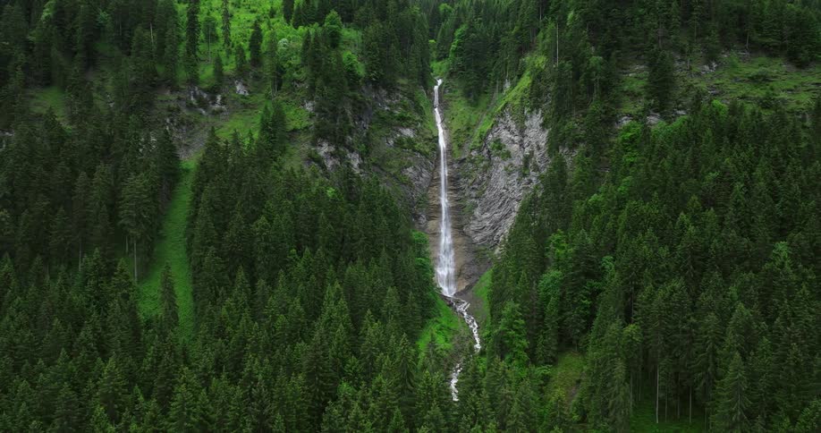 Waterfall flowing down the rugged surface of a cliff on the mountains surrounded by green lush vegetation