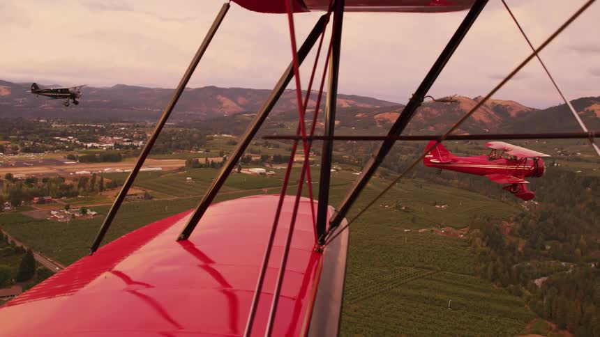 Two red biplanes are in the air over a small town