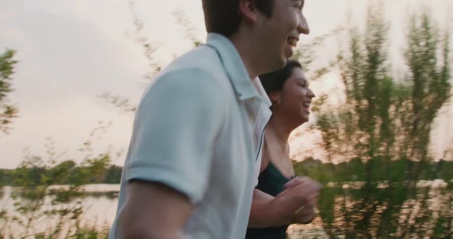 Man and woman hold hands and laugh as they run next to a lake