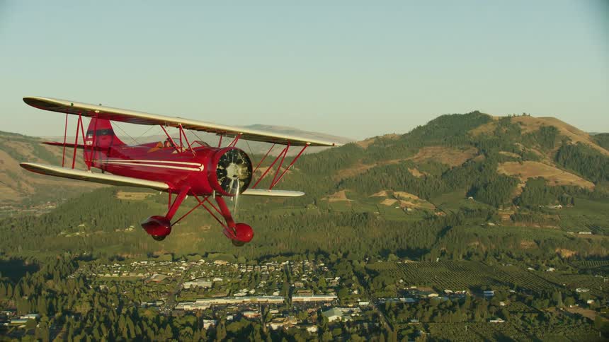 An red biplane is flying in the sky at sunset