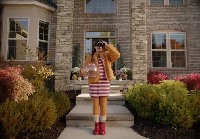 A kid is standing in front of a house and holding a fish bowl
