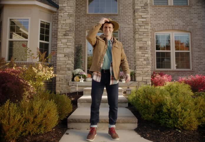 Happy smiling man standing in front of a house purposely puts on a hat