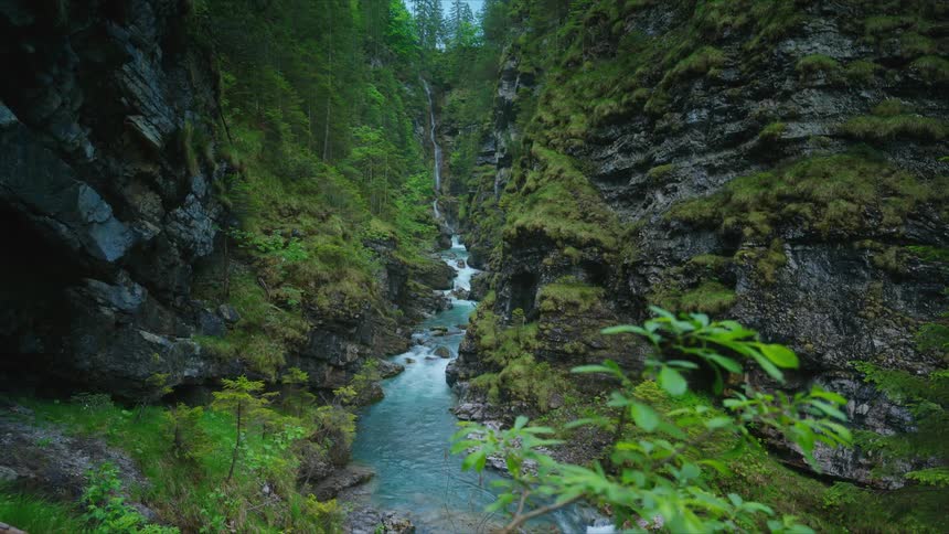 Water flows from a tall waterfall and into the stream and then continues on over the rocks