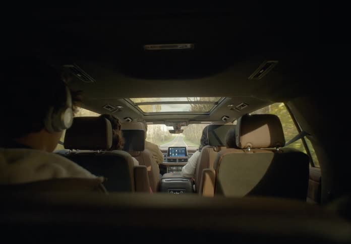 Mom looks back from the front passenger seat at the two rows of her kids while dad drives