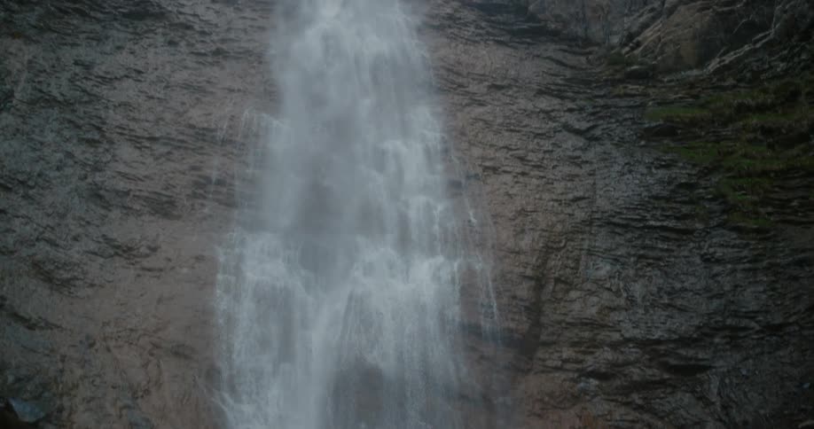 Tall waterfall flowing down the rugged barren rock surface of a cliff on the mountains