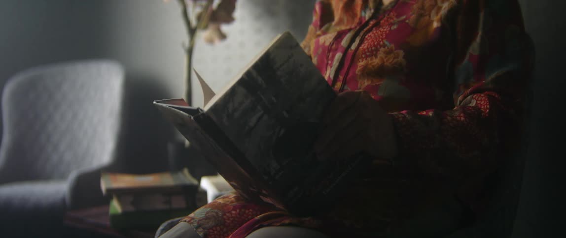 A person is sitting down indoors and reading a book