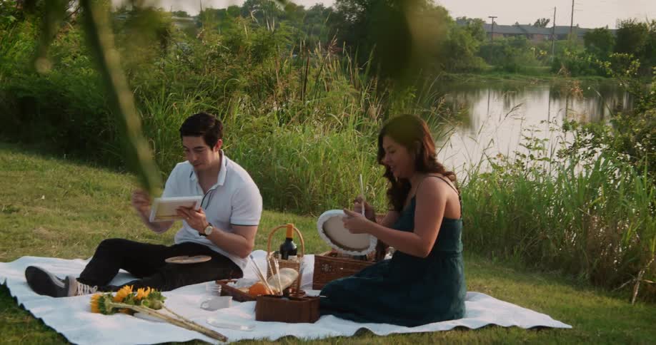 Young couple sitting over a blanket on the grass near a river painting with oils on small canvases