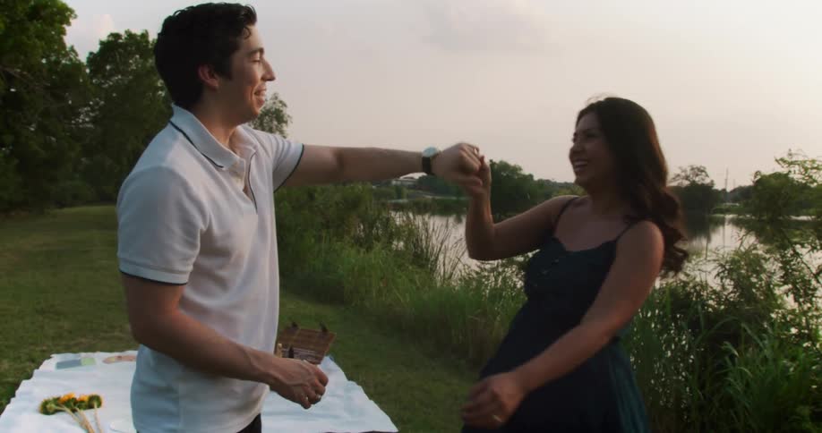 A man and woman are dancing near a lake where they are having a picnic