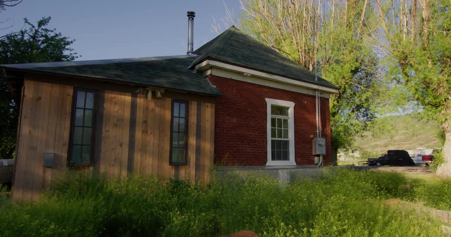 House sits on overgrown lot with vehicles parked nearby