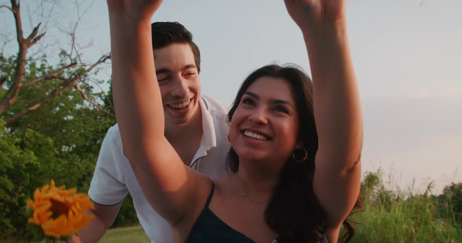A man gives his girlfriend and flower and kisses her cheek while she takes a selfie