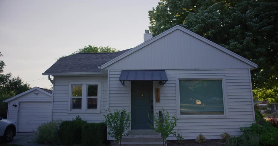 A small family home in a neighborhood with a large front window reflecting the street