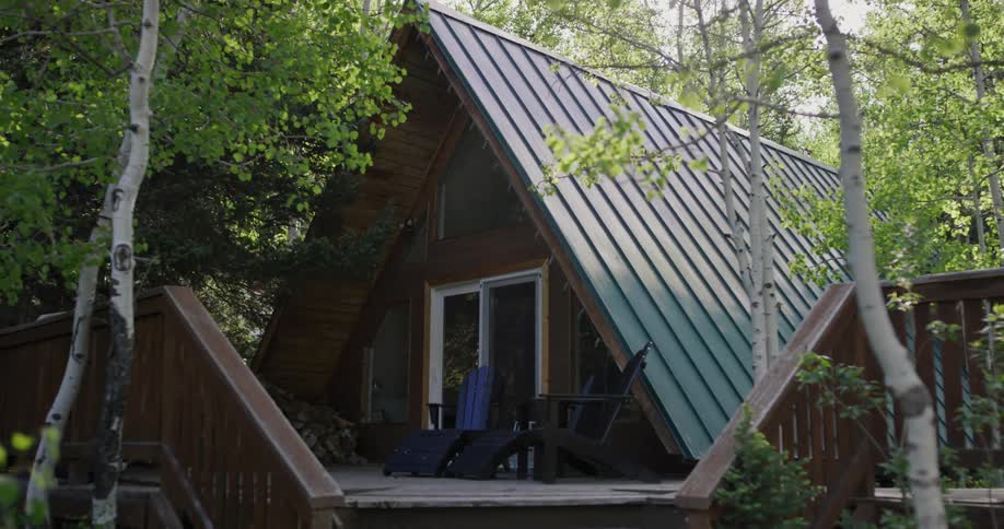 Chairs are sitting on the porch of a house in the woods surrounded by tall trees