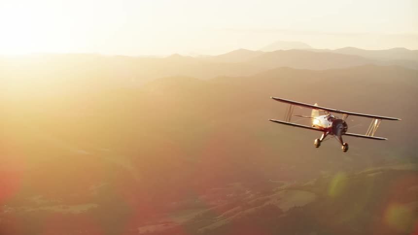 A red biplane flies into frame as the setting sun is in the background