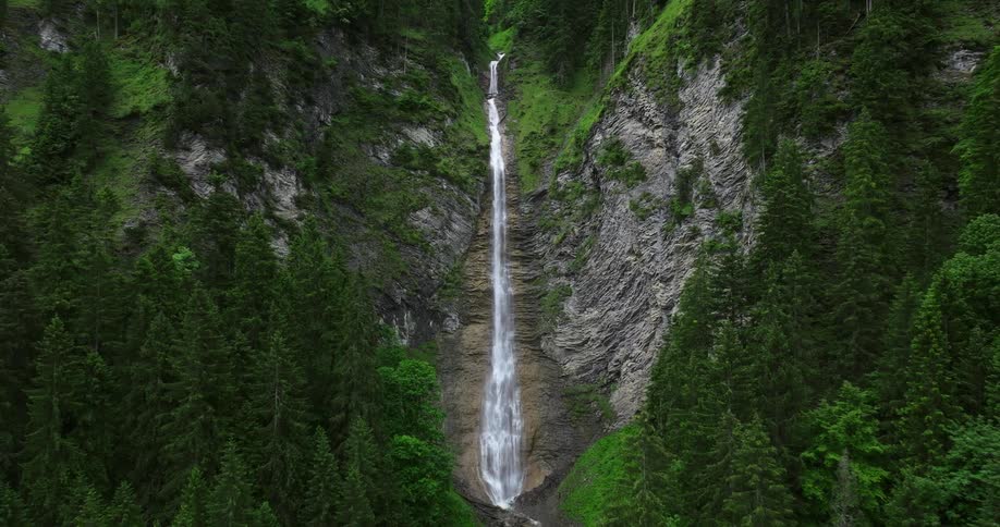 Water cascades down the side of a tree covered mountain