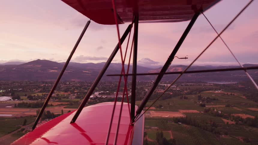 Two small red biplanes fly over a small rural town in the evening