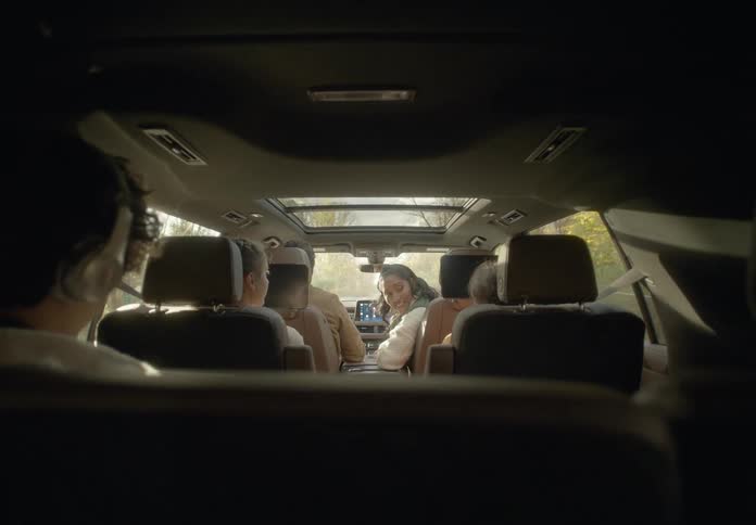 Mom turns around in the passenger seat smiling and talking with the kids as dad drives