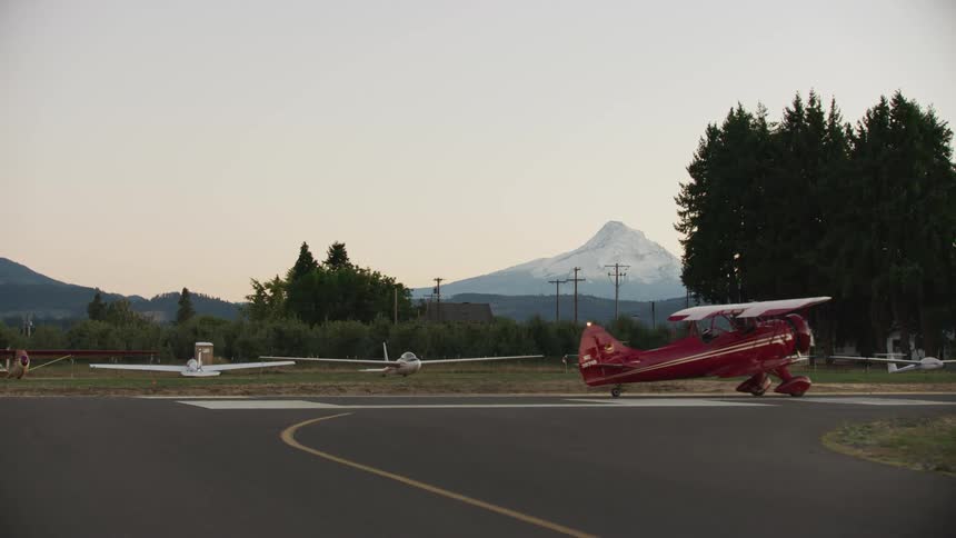 The red WACO biplane taxies over the runway on a small airport on a rural area with Mount Hood in the background