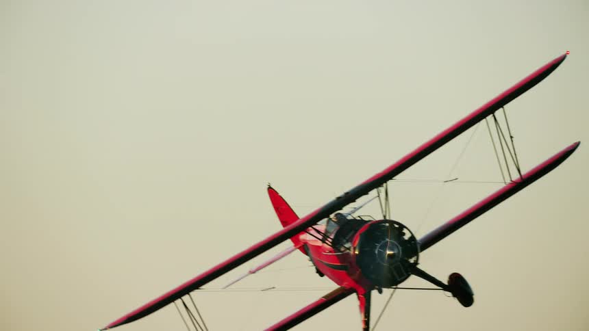 Aerial view of a red biplane flying low close to the mountains at morning