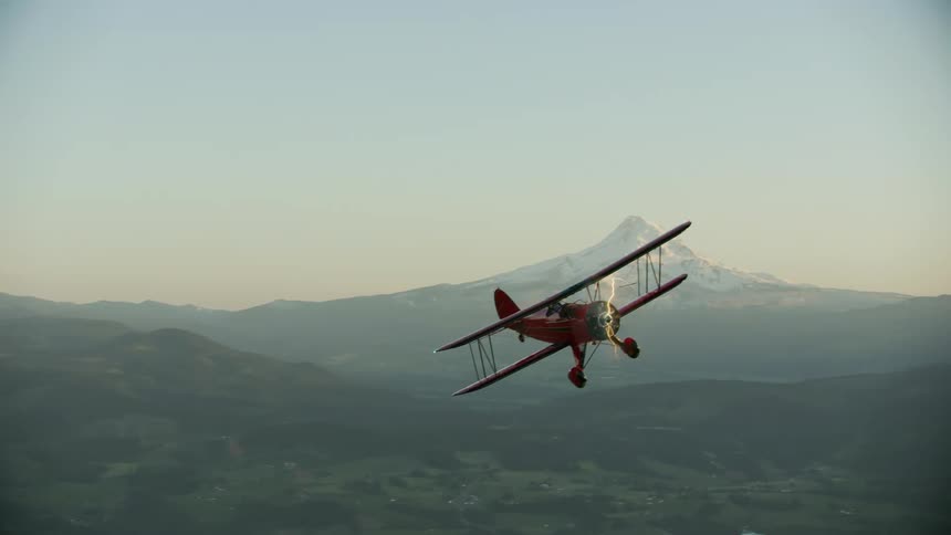 An airplane is flying over a wilderness area while the sun is setting
