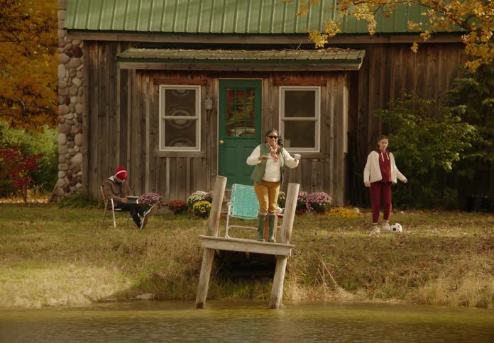 Young woman relaxing on a small wooden pier in front of a cabin spills coffee while greeting someone