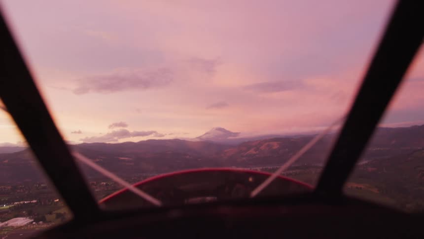 Pilot POV as the red WACO biplane flies straight towards a giant mountain at sunset