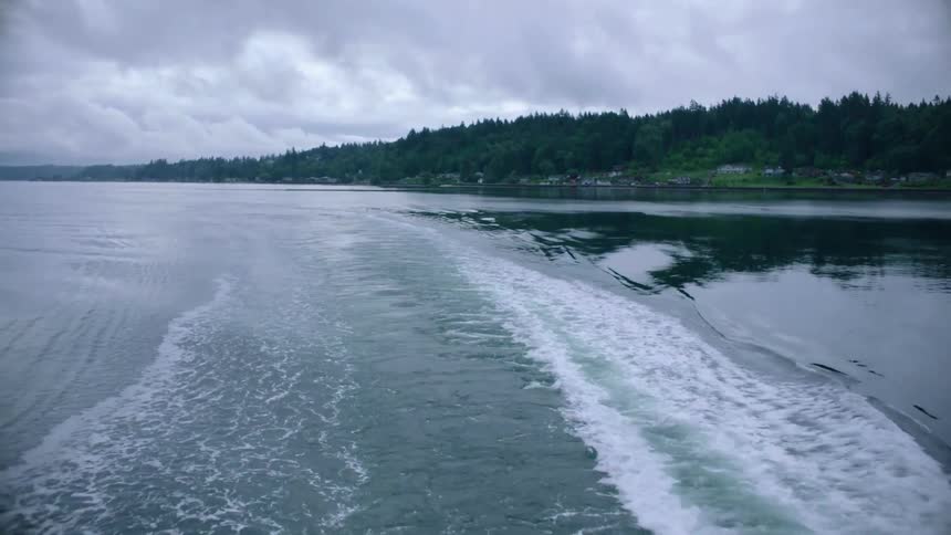 Boat travels on lake next to hill under cloudy sky