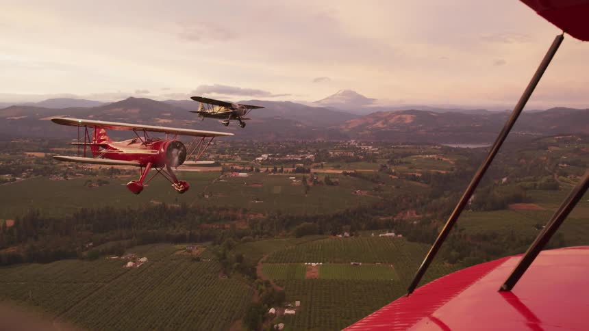 A squadron of old red biplanes flying over the fields near a small town at evening