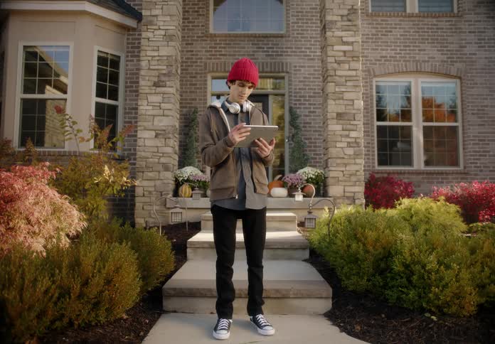 A teenager is standing outside of his house with a tablet
