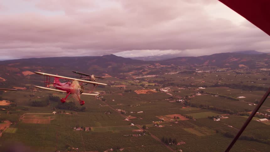 Three small radial engine biplanes fly over countryside with mountains in the background