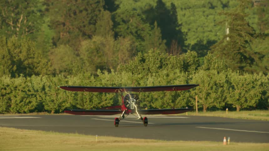 Small red airplane takes off from the runway with beautiful apple orchards in the background
