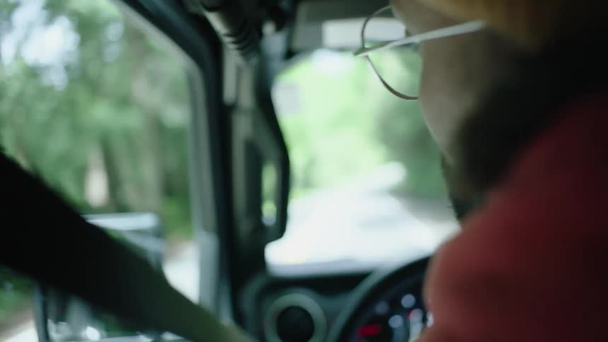 Woman with yellow hat glasses and curly hair drives van on forest road