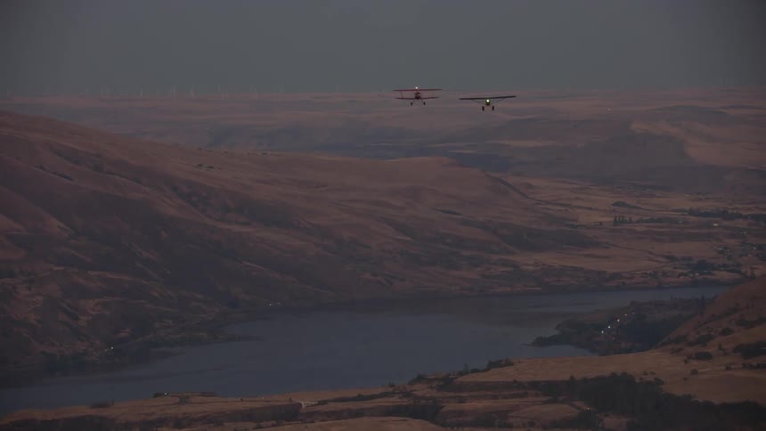 Two old planes flying low in front of a mountain over a river in the desert at evening
