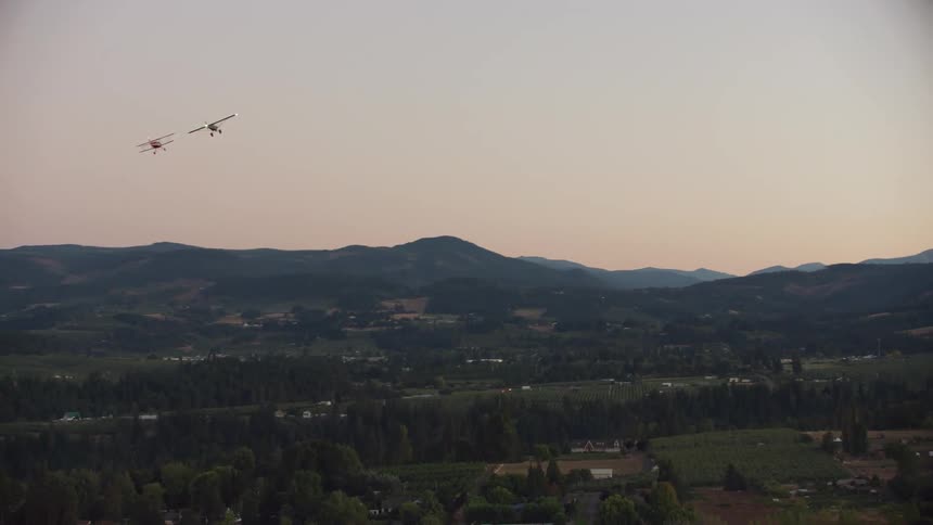 Two small planes fly over a neighborhood near a mountain range
